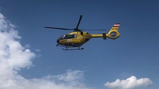 Ein gelber Hubschrauber mit der Registrierung OE-XVT fliegt durch einen blauen Himmel mit weißen Wolken.