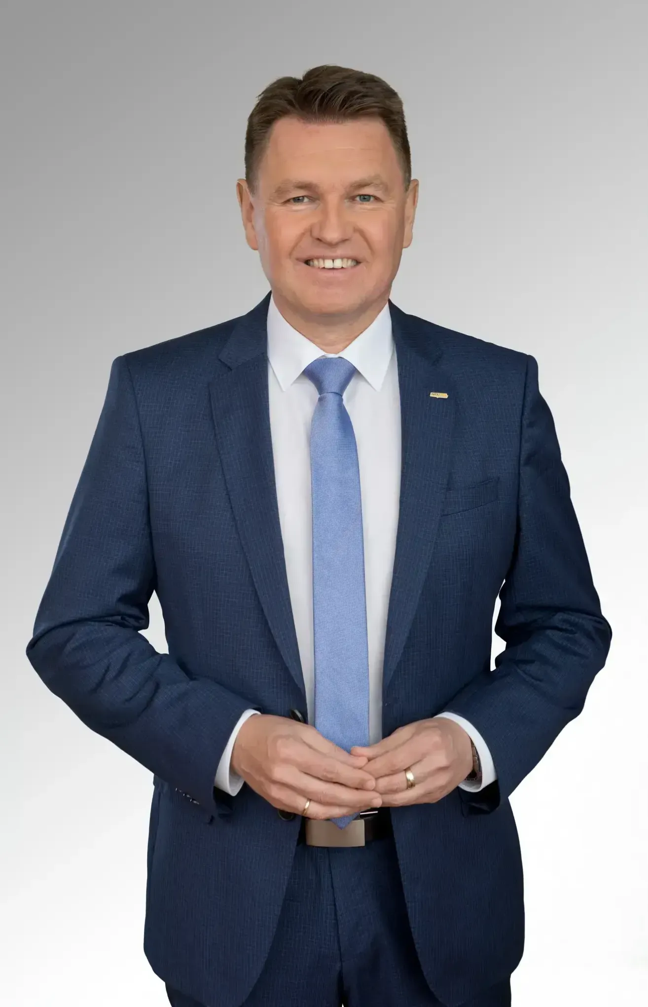 Ein Mann in einem blauen Anzug und einer Krawatte mit einem weißen Hemd darunter. Er lächelt und posiert für ein Foto.