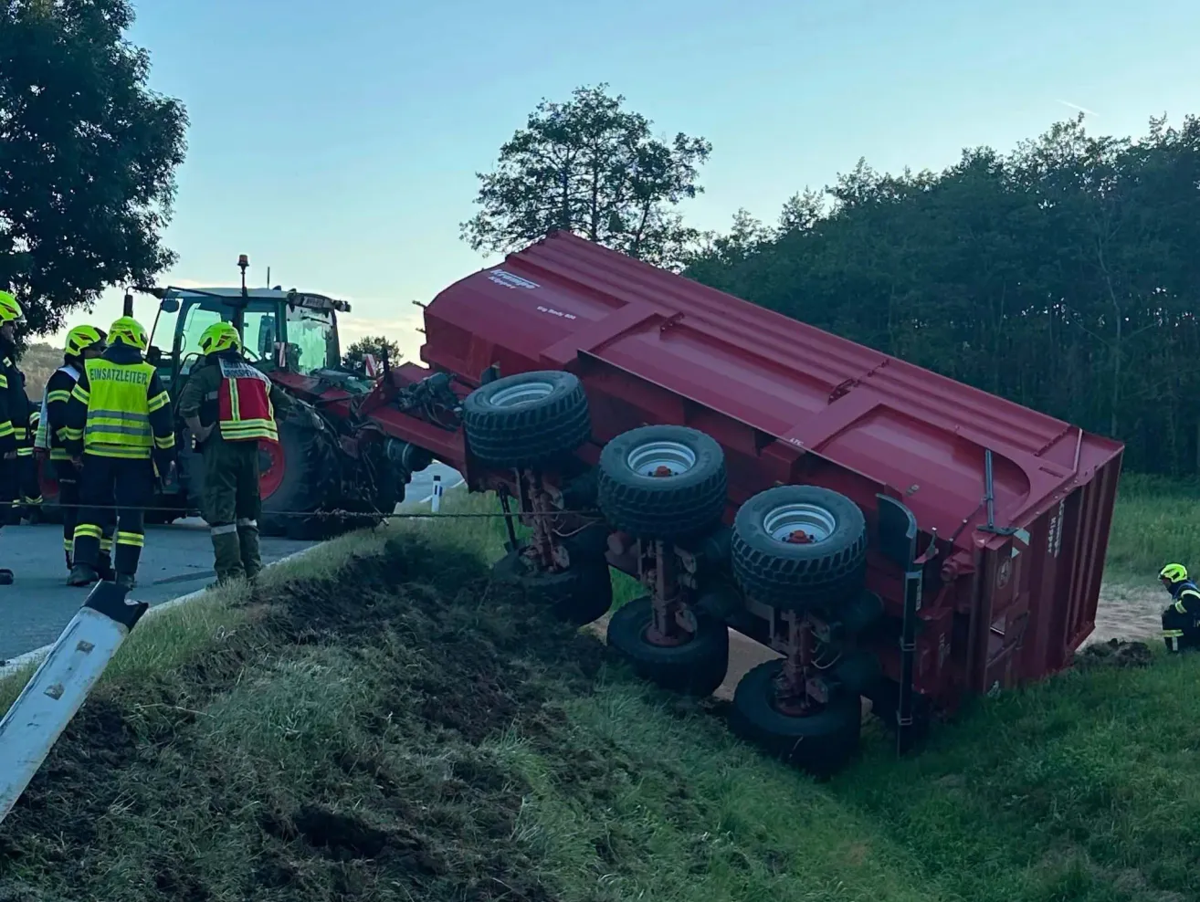 Ein roter LKW mit vier Rädern ist auf der Straßenseite umgekippt. Eine Person steht in der Nähe.