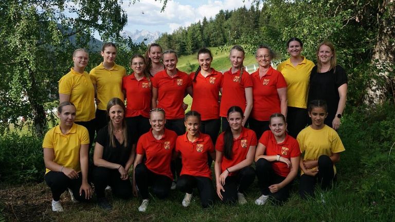 A group of women in red and yellow uniforms pose for a photo in a grassy area. They are all smiling and posing for the camera.