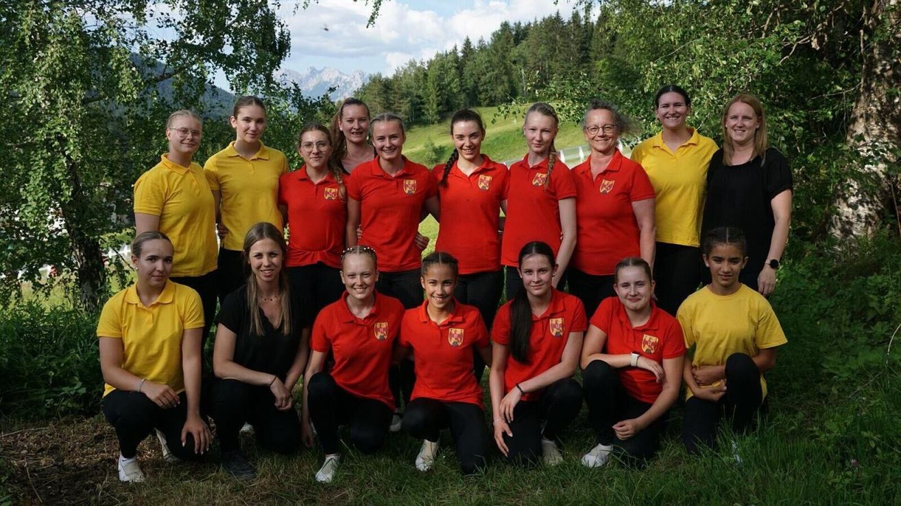 A group of women in red and yellow uniforms pose for a photo in a grassy area. They are all smiling and posing for the camera.