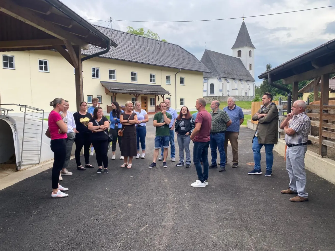 A group of people are gathered in front of a building with a church behind. They appear to be talking to someone.