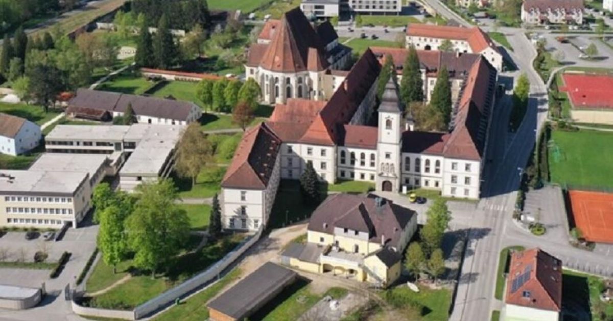 Ein Luftbild einer alten Klosteranlage mit roten Dächern und einem Kirchturm in einer üppigen grünen Umgebung.
