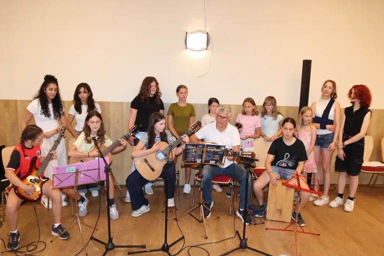 A group of children and an older man are playing guitars in a room. They have music stands in front of them.