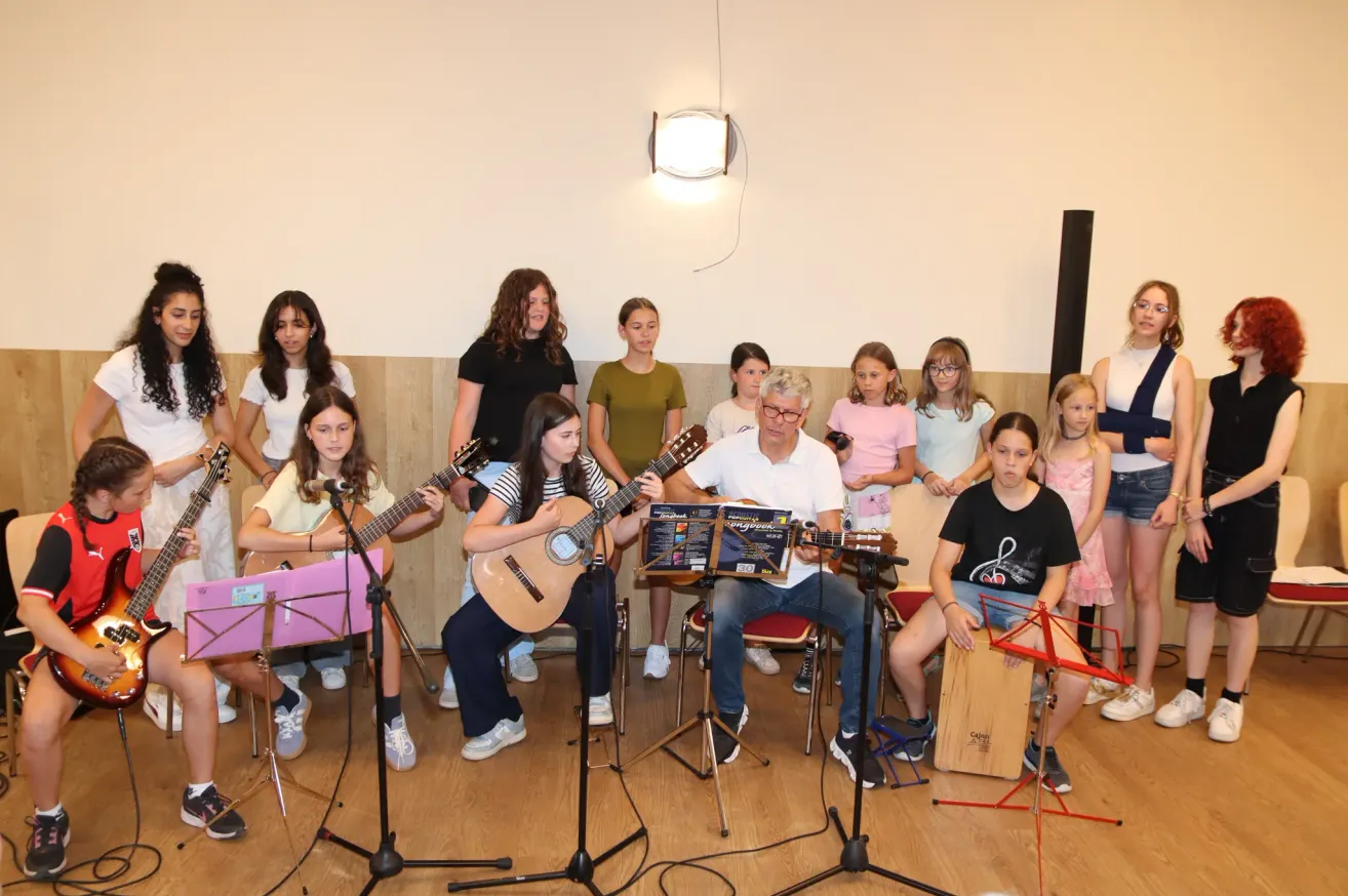 A group of children and an older man are playing guitars in a room. They have music stands in front of them.