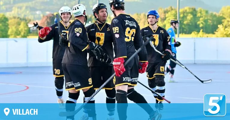 Eine Eishockeymannschaft in voller Ausrüstung, einschließlich Helmen und Handschuhen, steht auf dem Eisfeld, hält ihre Schläger in den Händen und unterhält sich. Die Trikots der Spieler tragen die Nummern 90, 59, 99, 75 und 7.
