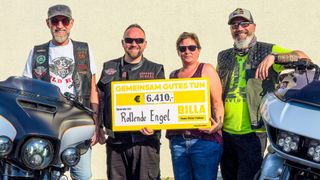 Vier Menschen stehen vor einer weißen Wand und lächeln. Ein Mann in der Mitte hält ein gelbes Plakat mit einer Spendenbotschaft und der Höhe von 6.410 Euro. Eine andere Person hält ein Schild. Hinter ihnen steht ein Motorrad.