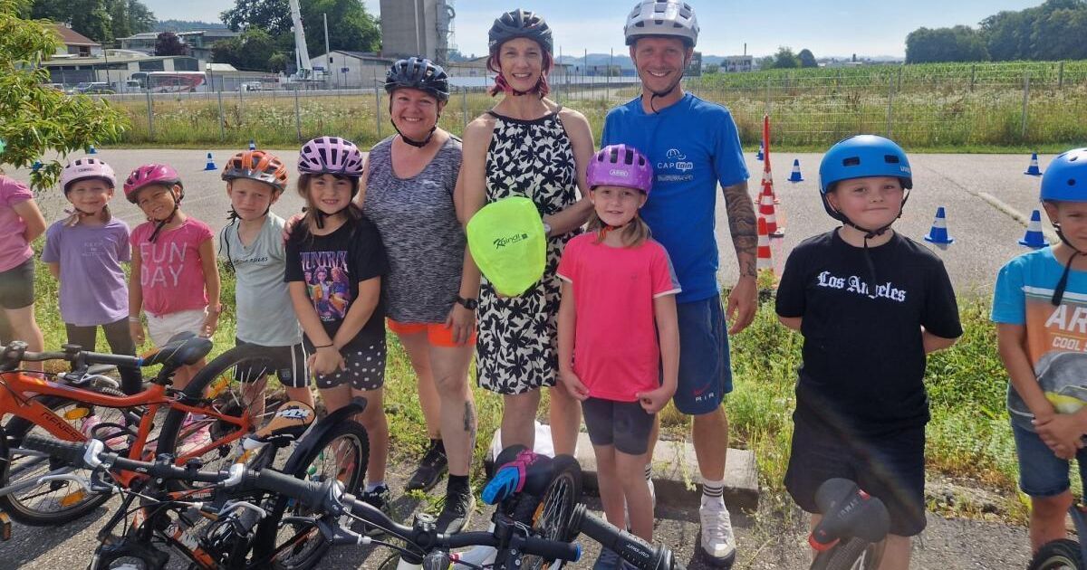 Eine Familie mit fünf Personen, darunter zwei Erwachsene und drei Kinder, posiert mit Fahrrädern in einem Grasbereich. Sie tragen alle Helme.