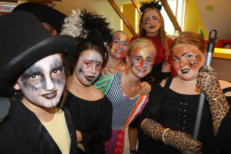 A group of young girls dressed in Halloween costumes with face paint are posing for a photo. They have spider webs, butterflies, and other designs on their faces.