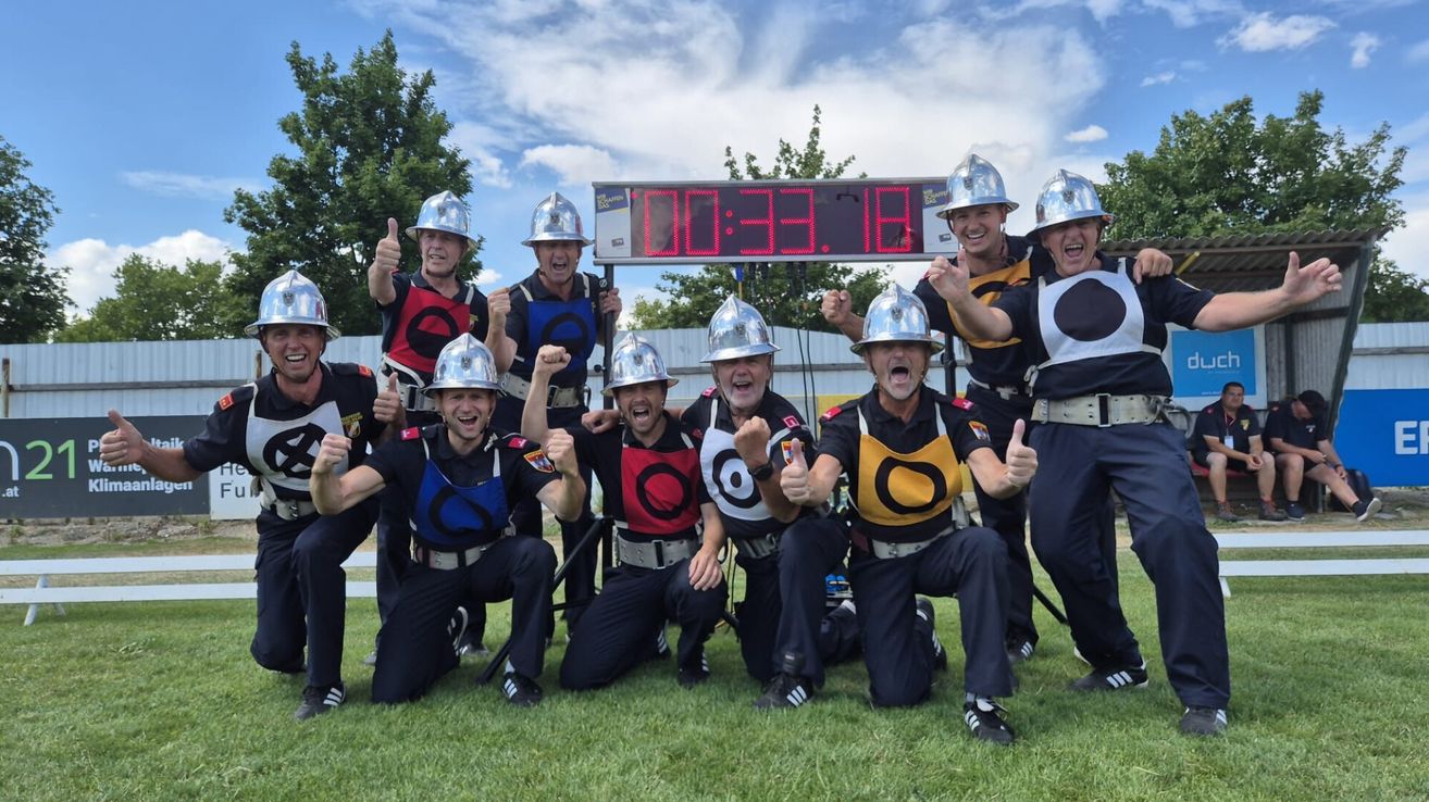 A group of firefighters pose for a photo with a digital timer showing 33.18 seconds, dressed in uniforms and helmets.