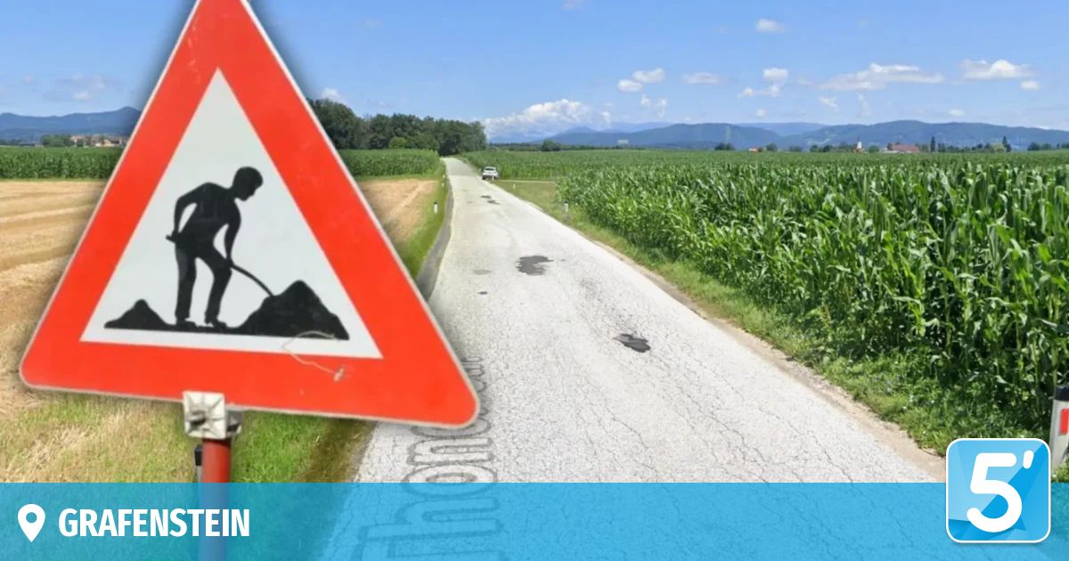 A road sign with a silhouette of a man digging on a rural road. The road is cracked and flanked by cornfields. Mountains are in the distance.