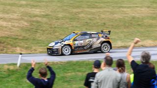 Ein Rallyeauto mit der Nummer 33 rast auf einer Rennstrecke, während Zuschauer jubeln.