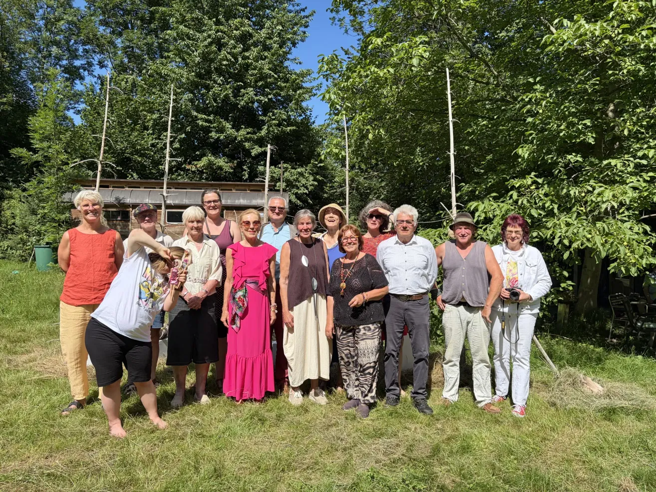 A group of people, both men and women, are standing in a grassy area, possibly for a group photo. They are all smiling and seem to be posing for the camera.