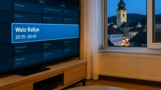 Ein Flachbildfernseher zeigt das Wort ally auf einem blauen Hintergrund. Die Zeit ist 0:45. Der Fernseher steht auf einem Holzständer. Ein Fenster mit einem weißen Vorhang befindet sich hinter dem Fernseher.
