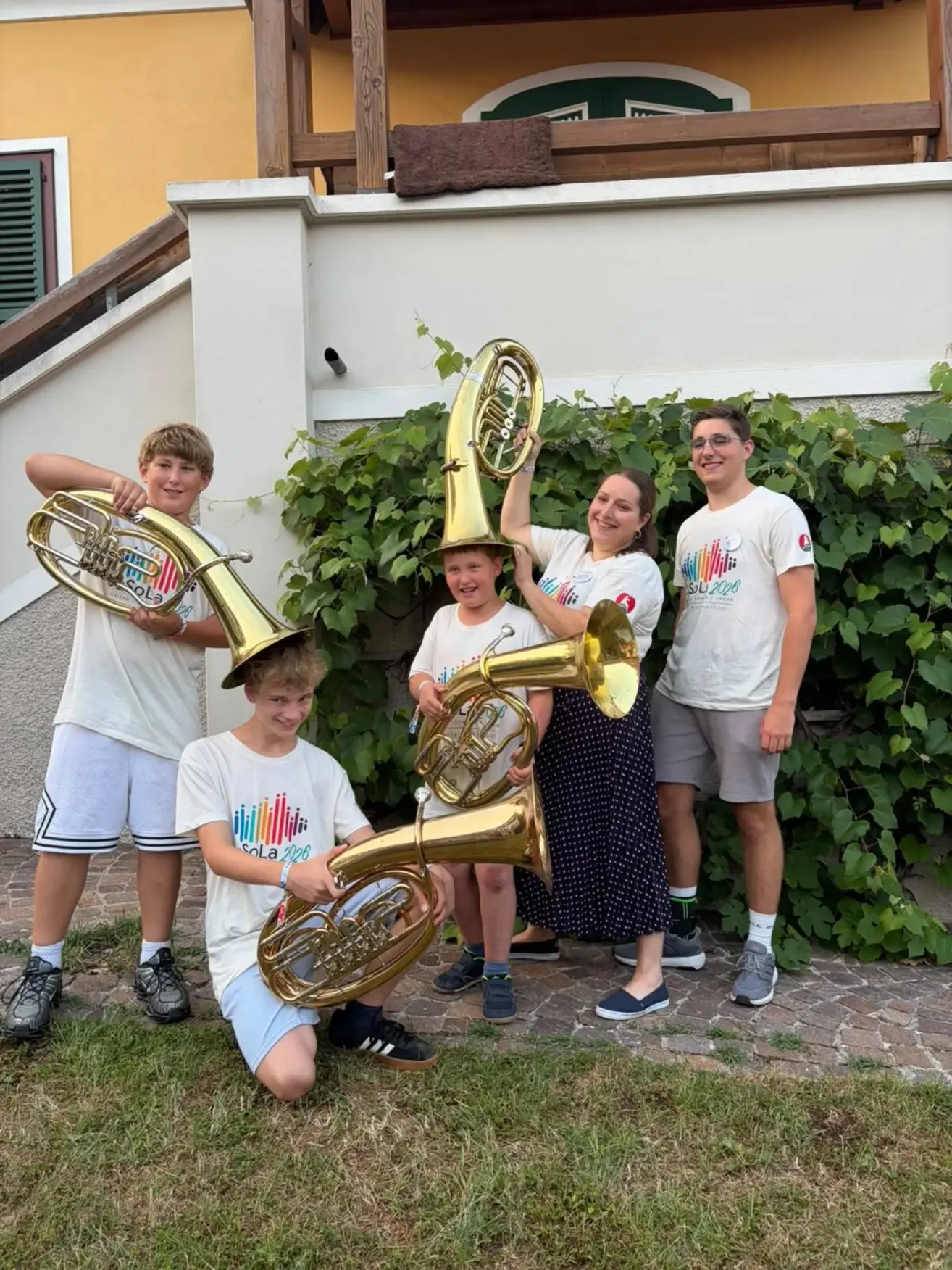 Eine fünfköpfige Familie posiert mit ihren Blechblasinstrumenten vor einem Haus mit einer grünen Pflanze.