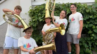 Eine fünfköpfige Familie posiert mit ihren Blechblasinstrumenten vor einem Haus mit einer grünen Pflanze.