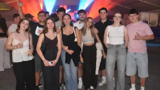 Eine Gruppe junger Erwachsener posiert für ein Foto bei einer nächtlichen Veranstaltung mit bunten Lichtern im Hintergrund.