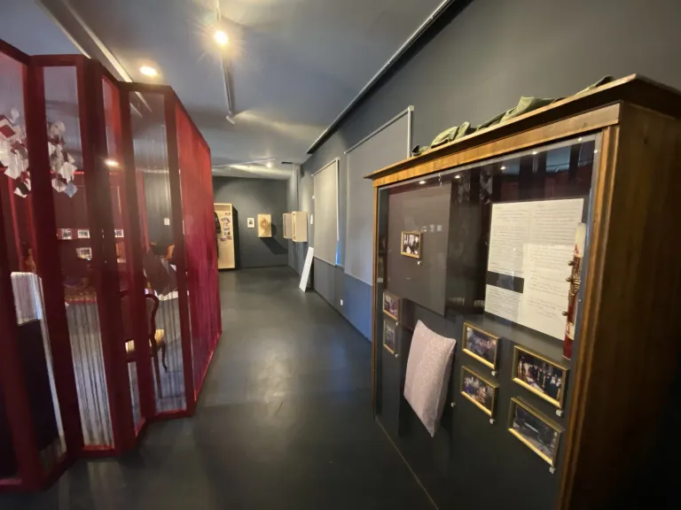 Ein leerer Flur mit einer roten Trennwand auf der linken Seite und einer Vitrine auf der rechten Seite, die gerahmte Fotos und ein Kissen enthält.