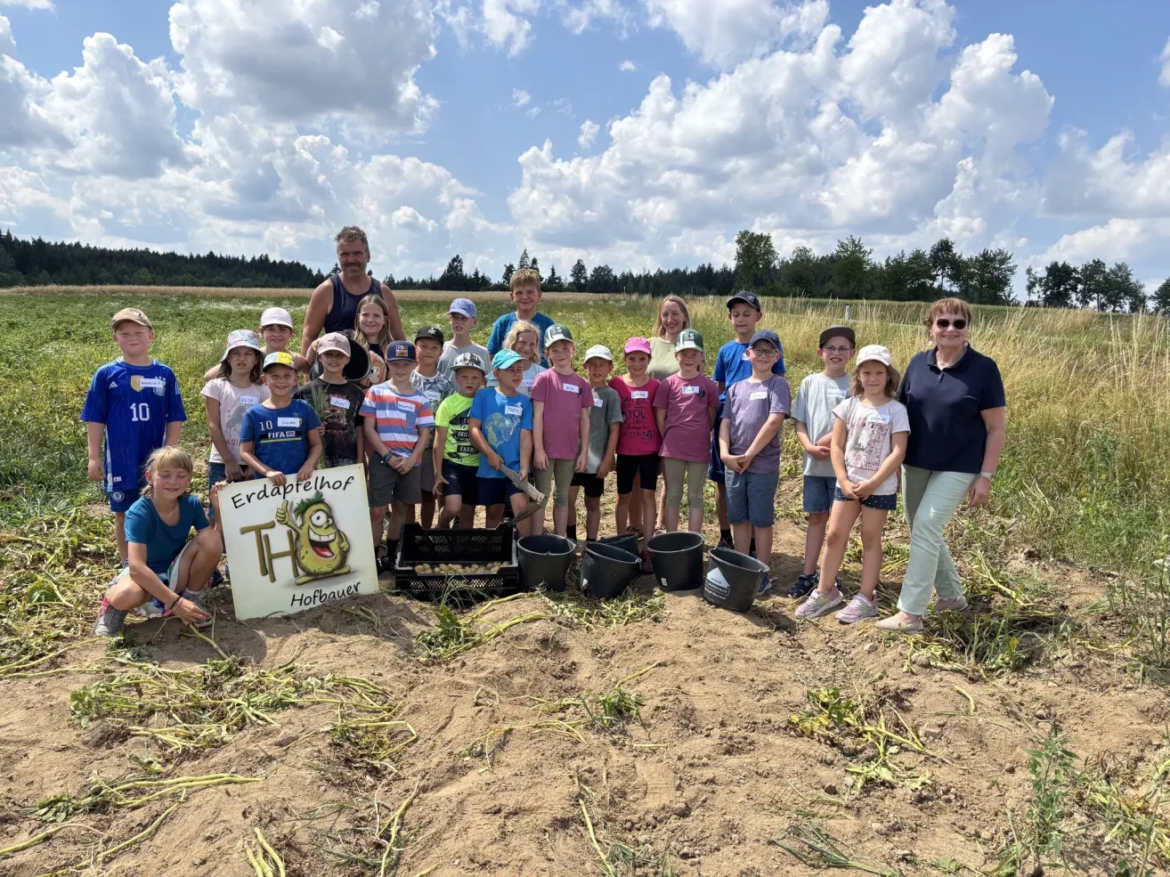 A group of children and adults are standing in a field with buckets, wearing hats and some holding a sign that says 'Erdapplehof'.