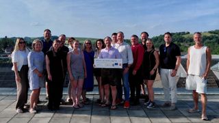 Eine Gruppe von lässig gekleideten Menschen posiert für ein Foto auf einem Dach mit einem großen Scheck, der Wirtschaft meets Jugend 2.0 in der Mitte beschriftet ist.