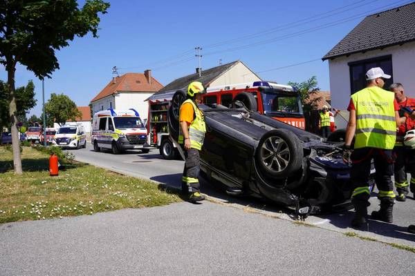 Rettungsdienste kümmern sich um ein umgekipptes Auto am Straßenrand. Arbeiter in gelben Westen stehen um das Fahrzeug herum.