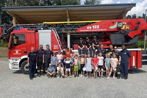 A group of firefighters and children pose for a photo in front of a red fire truck.