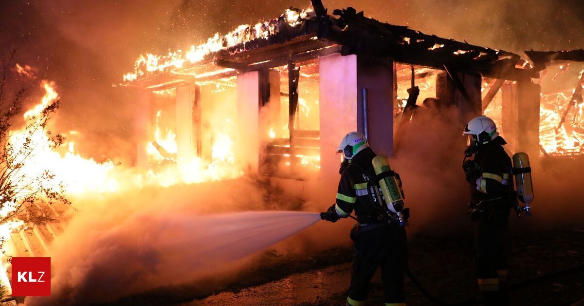Ein Feuerwehrmann in voller Ausrüstung sprüht Wasser aus einem Schlauch, um ein brennendes Haus zu löschen.