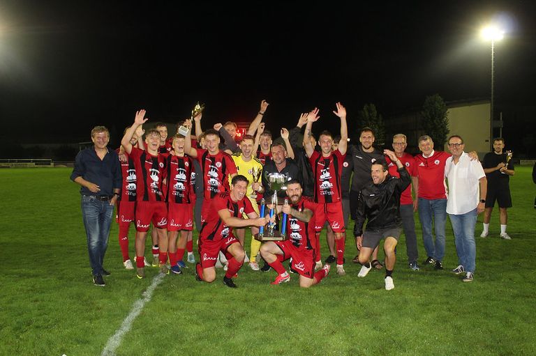Eine Fußballmannschaft feiert auf dem Feld bei Nacht, hält Trophäen und jubelt.