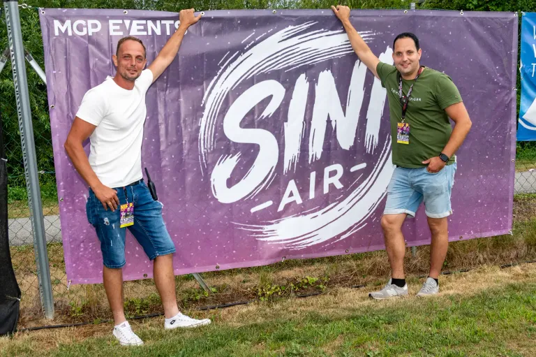 Zwei Männer stehen neben einem Banner für das Sin Air Event, beide lächeln und posieren für ein Foto.