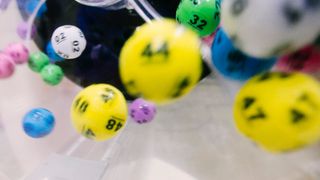A close-up view of various colored dice with numbers ranging from 02 to 87, some in motion, inside a transparent container.