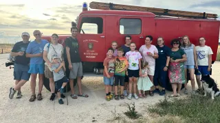 A group of people, including adults and children, are posing for a photo in front of a red fire truck.