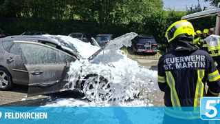 A firefighter is using a foam extinguisher on a damaged car in a parking lot, with several other cars parked nearby.
