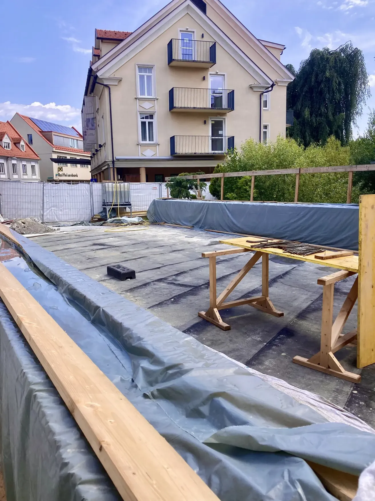 A construction site with a wooden table and tarps on a rooftop, with a building with solar panels in the background.
