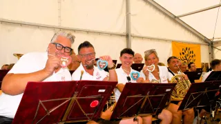 A group of musicians in white shirts are posing for a photo with heart-shaped cookies in their hands. They are sitting on chairs with music stands in front of them.