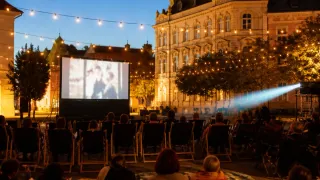 Eine Outdoor-Filmvorführung findet bei Nacht vor einem historischen Gebäude statt, mit Leuten, die in Klappstühlen unter Lichterketten sitzen.