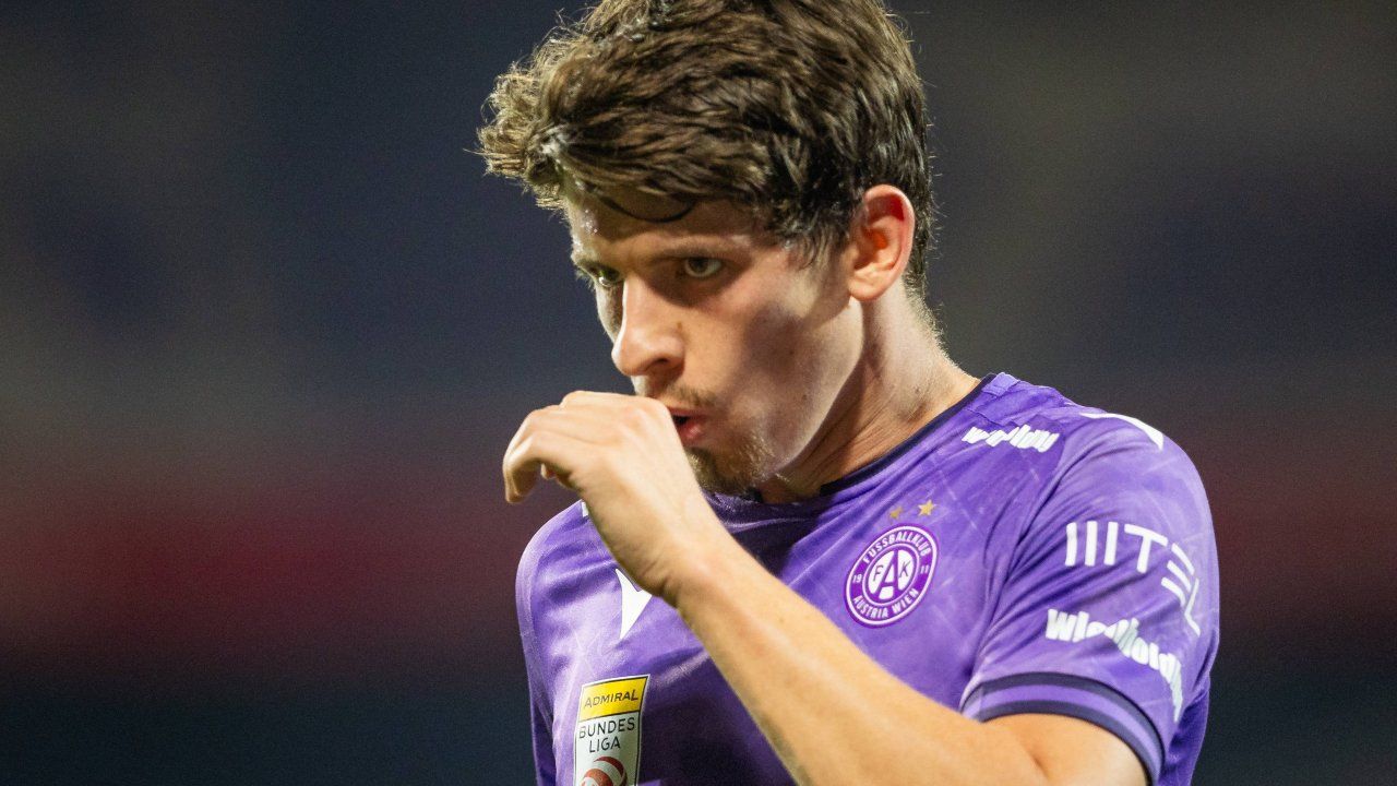 A soccer player in a purple jersey with the number 11 on it is looking to the left with his hand on his mouth.