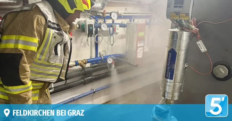 A firefighter in full gear is using a device to spray water in a room with industrial equipment and pipes. The room has a blue background with the text 'HEN BEI GRAZ'.