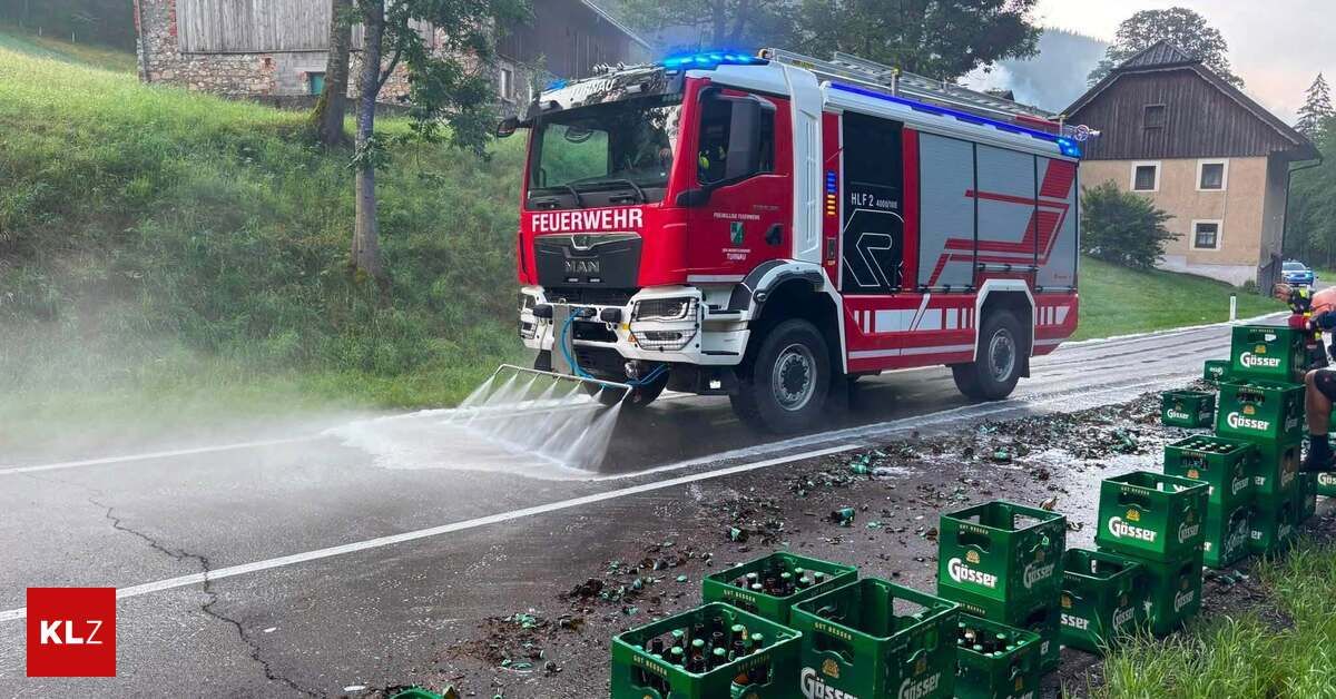 Ein roter Feuerwehrwagen mit 'Feuerwehr' beschriftet sprüht Wasser auf die Straße, mit verstreuten Bierflaschen und grünen Kisten in der Nähe.