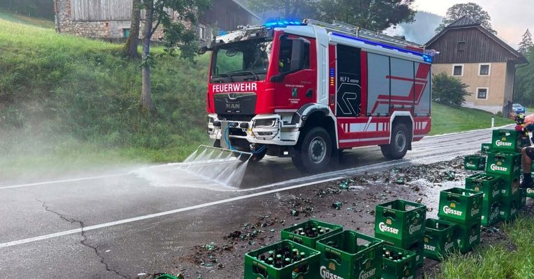 Ein roter Feuerwehrwagen mit blauen Lichtern sprüht Wasser auf eine Straße, mit mehreren Bierkisten und Flaschen auf dem Boden verstreut.