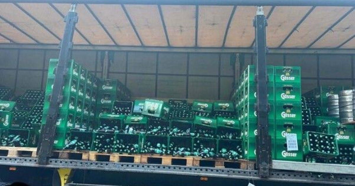 Ein LKW ist mit zahlreichen grünen Kisten beladen, die jeweils Flaschen eines Getränks enthalten. Die Kisten sind in Reihen gestapelt und die Flaschen sind durch die Öffnungen der Kisten sichtbar.