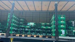 Ein LKW ist mit zahlreichen grünen Kisten beladen, die jeweils Flaschen eines Getränks enthalten. Die Kisten sind in Reihen gestapelt und die Flaschen sind durch die Öffnungen der Kisten sichtbar.