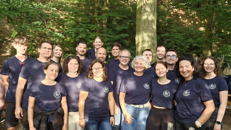 Eine Gruppe von Menschen in passenden marineblauen T-Shirts posiert für ein Foto im Wald.