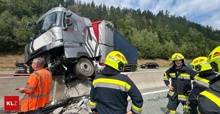 Ein LKW ist auf einer Autobahn in eine Betonbarriere geprallt. Zwei Feuerwehrleute in gelben Helmen stehen in der Nähe.