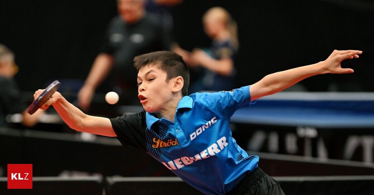 Ein junger Junge in einem blauen Shirt mit den Worten 'Strick' und 'Donic' spielt Tischtennis und schlägt einen Ball mit seinem Schläger. Im Hintergrund beobachten zwei Personen das Spiel.