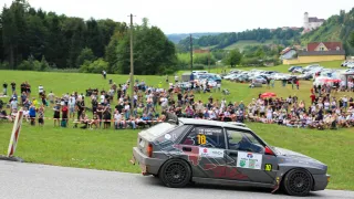 A rally car with number 10 on the side is driving on a road with a crowd of people watching from the side.