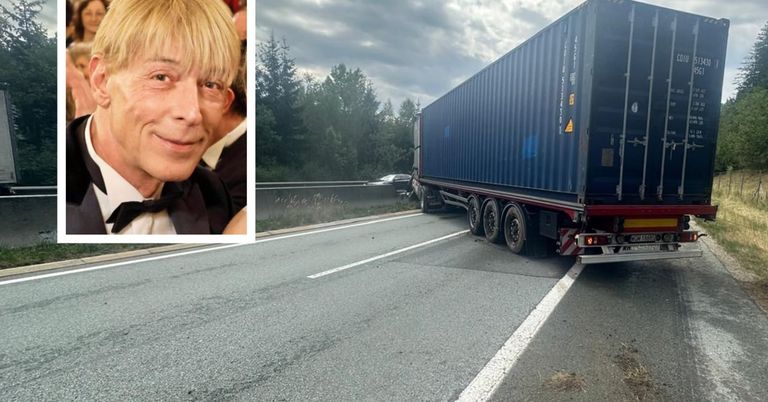 Ein Mann mit blondem Haar und einer Fliege lächelt in die Kamera. Daneben steht ein blauer LKW am Straßenrand.