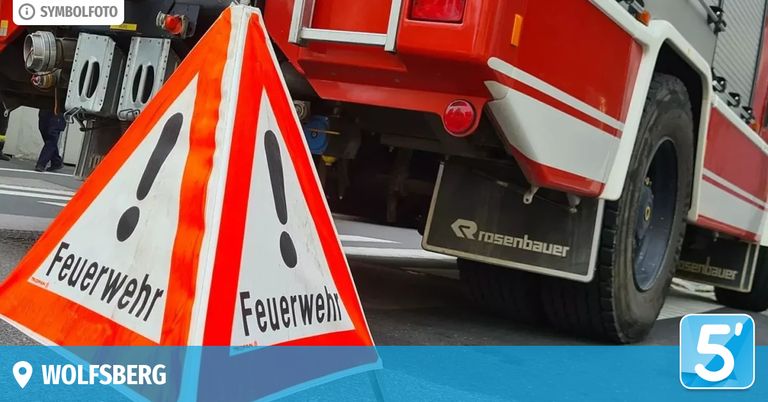 A red fire truck with a warning sign that reads 'Feuerwehr' in German. The sign is triangular with a red and white background and black exclamation marks.