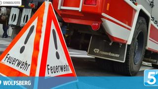 A red fire truck with a warning sign that reads 'Feuerwehr' in German. The sign is triangular with a red and white background and black exclamation marks.