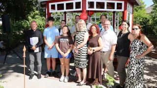 A group of people, including adults and children, are standing in front of a red gazebo with hanging lanterns. They appear to be posing for a photo.