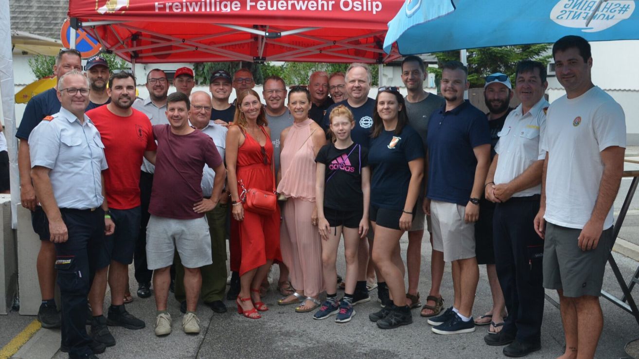 Eine Gruppe von Menschen, darunter Männer und Frauen, steht unter einem Zelt mit einem roten Baldachin. Sie alle lächeln und posieren für ein Foto.